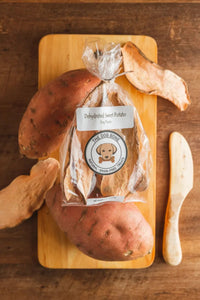 Bag of dehydrated sweet potatoes with fresh sweet potatoes on a wooden cutting board
